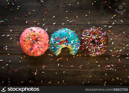 Colorful tasty sparkled donuts on a wooden background. Perfect for dessert-related post and articles. Colorful tasty sparkled donuts on a wooden background