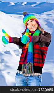 Colorful thumbs up of a happy smiling girl wearing winter clothes, beautiful female portrait, young pretty woman with natural snow background, winter fun outdoor, happy people concept