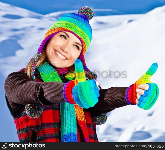 Colorful thumbs up of a happy smiling girl wearing winter clothes, beautiful female face portrait, young pretty woman with natural snow background, winter fun outdoor, happy people concept
