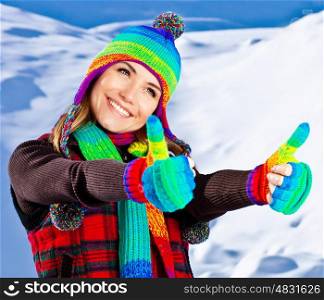 Colorful thumbs up of a happy smiling girl wearing winter clothes, beautiful female face portrait, young pretty woman with natural snow background, winter fun outdoor, happy people concept