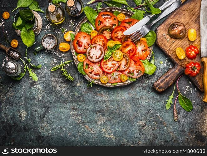 Colorful tomatoes salad preparation with cutting board, plate and cutlery , top view, border