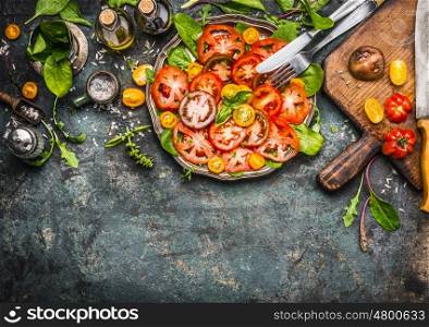 Colorful tomatoes salad preparation with cutting board, plate and cutlery , top view, border