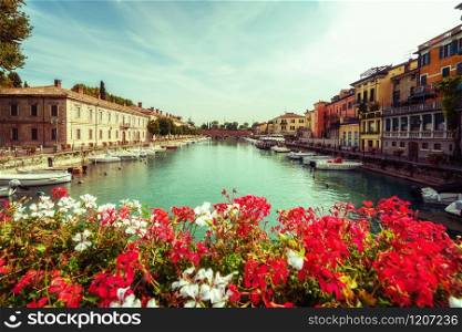 Colorful town of Peschiera del Garda with boats and blurred geranium flowers. The city is located at lake Lago di Garda,East of Venice, Italy, Europe.. Colorful town of Peschiera del Garda in Italy.