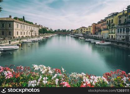Colorful town of Peschiera del Garda with boats and blurred geranium flowers. The city is located at lake Lago di Garda,East of Venice, Italy, Europe.