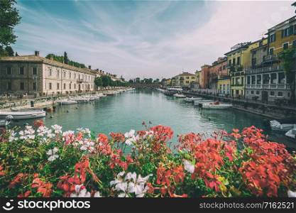 Colorful town of Peschiera del Garda with boats and blurred geranium flowers. The city is located at lake Lago di Garda,East of Venice, Italy, Europe.. Colorful town of Peschiera del Garda in Italy.