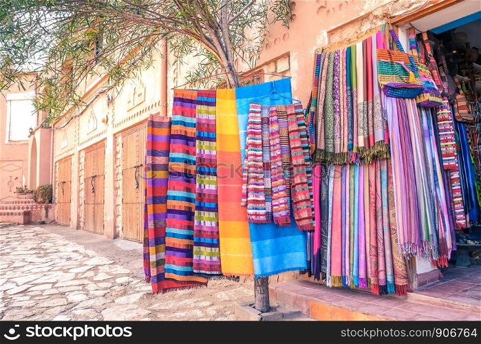 Colorful traditional Moroccan scarves and shawls hanging on a tree for sale at a souvenir shop in Ouarzazate, Morocco.