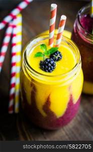 Colorful two layer smoothies with mango and berries on rustic wooden background