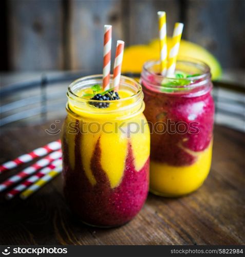 Colorful two layer smoothies with mango and berries on rustic wooden background