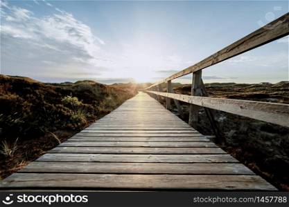 Colorful view of seaside landscape before sunset. Low view of Wooden touristic walkway with railing leading to sun. Summer vacation and wildlife concept.