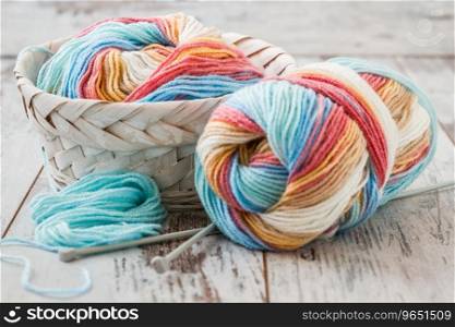 Colorful woolen knitting yarns in white basket on white wooden table