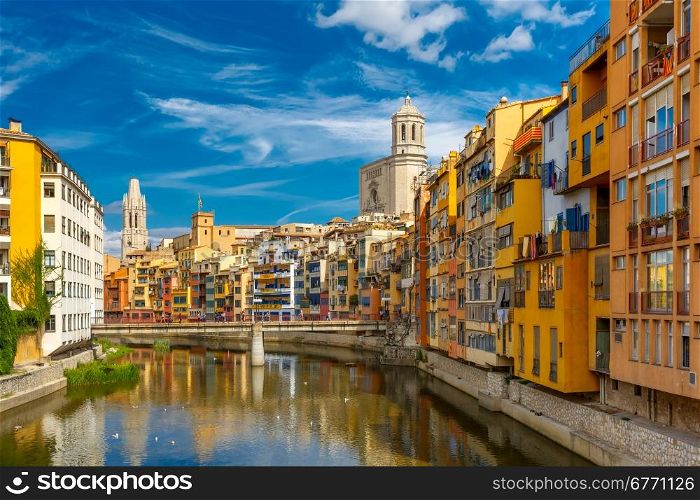 Colorful yellow and orange houses and bridge Pont de Sant Agusti reflected in water river Onyar, in Girona, Catalonia, Spain. Church of Sant Feliu and Saint Mary Cathedral at background.
