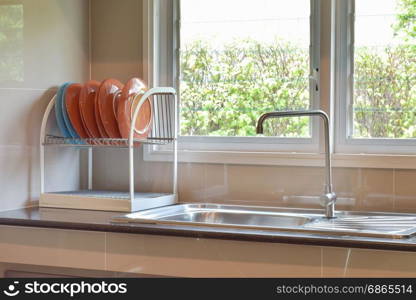 Colorfull plates on shelf next to sink on black marble top with natural light