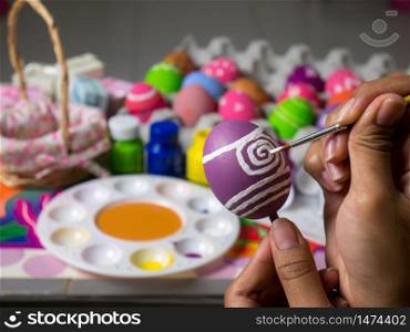 Coloring eggs with various colors beautifully with the brush during the Easter. Woman paint on easter eggs. Beautiful art on eggs in easter festival.