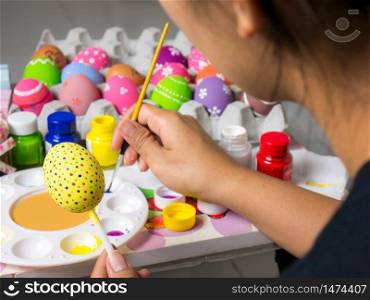 Coloring eggs with various colors beautifully with the brush during the Easter. Woman paint on easter eggs. Beautiful art on eggs in easter festival.
