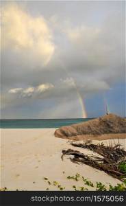Colourful rainbow over the sea with waves and rocks on the tropical beach Petite Anse under a stormy sky, La Digue Island, Indian Ocean, Seychelles