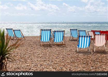 Colourful striped deck chairs for rent on the pebble beach at Brighton, East Sussex, England