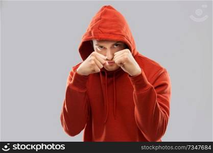 combat, aggression and people concept - young man in red hoodie fighting with fists or boxing over grey background. man in red hoodie fighting with fists or boxing