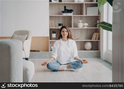 Comfort and serenity. Relaxed hispanic woman is practicing yoga and meditation on floor at home. Lotus pose, morning gymnastics, body and soul in harmony. Concentration and consciousness concept.. Comfort and serenity. Relaxed hispanic woman is practicing yoga and meditation on floor at home.