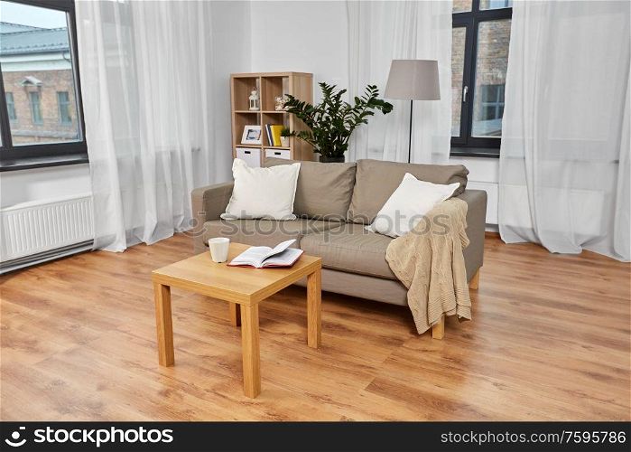 comfort, furniture and interior concept - sofa with cushions, coffee and book on table at cozy home living room. sofa, coffee and book on table at cozy home
