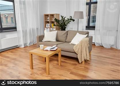 comfort, furniture and interior concept - sofa with cushions, coffee and book on table at cozy home living room. sofa, coffee and book on table at cozy home