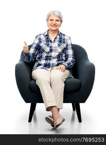 comfort, furniture and old people concept - smiling senior woman sitting in modern armchair and showing thumbs up over white background. old woman sitting in chair and showing thumbs up