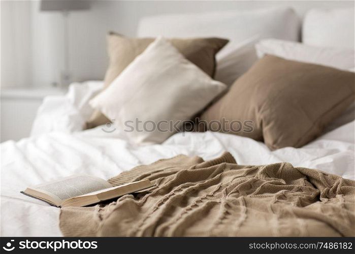 comfort, hygge and interior concept - cozy bed with pillows, blanket and open book at home. bed with pillows, blanket and open book at home