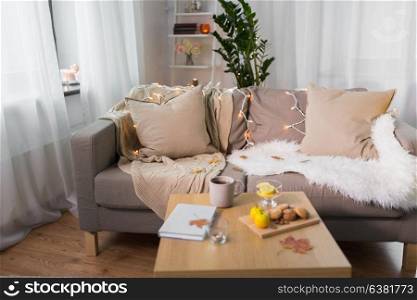 comfort, hygge, cozy home and interior concept - sofa with cushions and garland lights in living room. sofa with cushions at cozy home living room