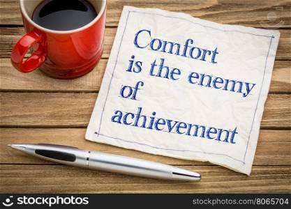 Comfort is the enemy of achievement - handwriting on a napkin with a cup of espresso coffee