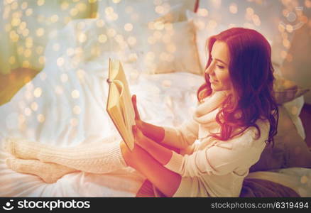 comfort, leisure and people concept - happy young woman reading book in bed at home bedroom. happy young woman reading book in bed at home