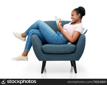 comfort, people and furniture concept - happy smiling young african american woman sitting in modern armchair writing to notebook over white background. happy young woman in armchair writing to notebook