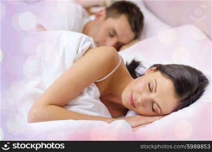 comfort, relationships and rest concept - happy couple sleeping in bed over holidays lights background