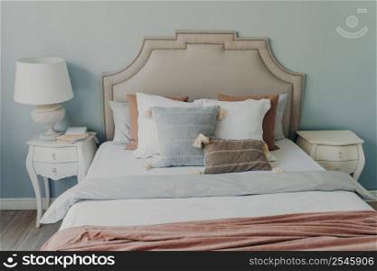 Comfortable bedroom interior and textile. Soft pillows on bed. Lamp on nightstand, bedsheets and blanket on the bed. Daytime interior. Concept of rest at home and relaxation in cozy room.. Comfortable bedroom interior and textile. Soft pillows on bed. Concept of rest at home in cozy room.