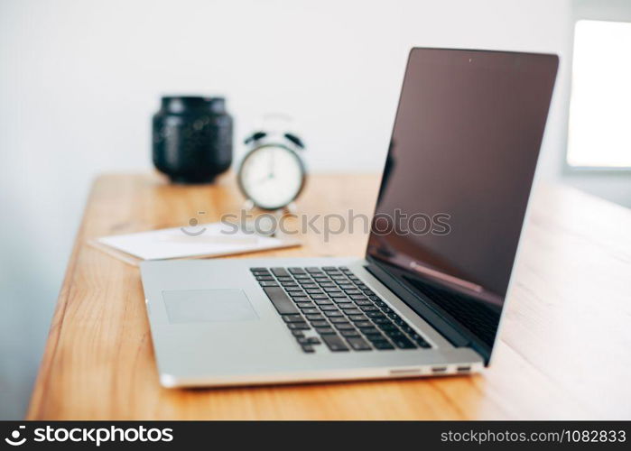 Comfortable working place in home office with wooden table and modern laptop laying on it. Freelance work concept