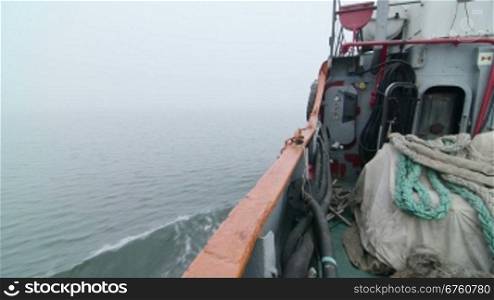 Commercial fishing boat moving forward in the misty sea of Azov