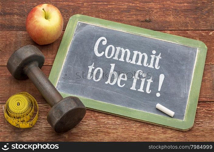 Commit to be fit concept - slate blackboard sign against weathered red painted barn wood with a dumbbell, apple and tape measure