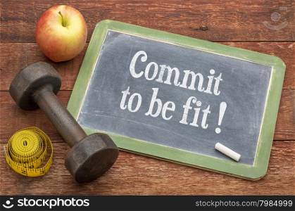 Commit to be fit concept - slate blackboard sign against weathered red painted barn wood with a dumbbell, apple and tape measure