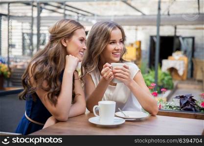 communication and friendship concept - smiling young women drinking coffee at street cafe. smiling young women drinking coffee at street cafe