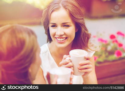 communication and friendship concept - smiling young women with coffee cups at cafe. smiling young women with coffee cups at cafe