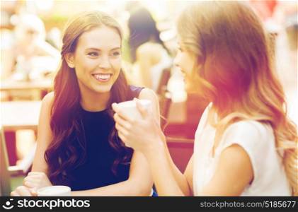 communication and friendship concept - smiling young women with coffee cups at cafe. smiling young women with coffee cups at cafe