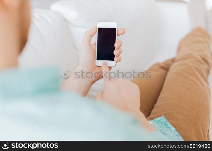 communication, business, home and technology concept - close up of man with smartphone texting message sitting on couch at home