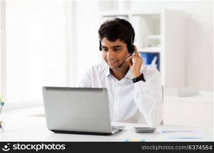 communication, business, people and technology concept - businessman or helpline operator with headset and laptop computer typing at office. businessman with headset and laptop at office