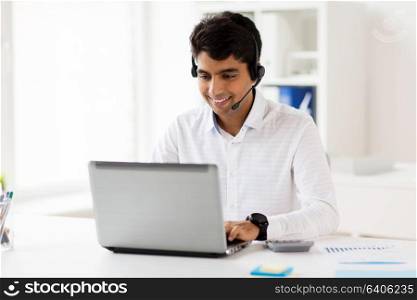 communication, business, people and technology concept - businessman or helpline operator with headset and laptop computer typing at office. businessman with headset and laptop at office