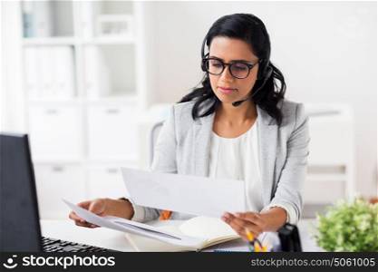 communication, business, people and technology concept - businesswoman or helpline operator with headset, computer and papers at office. businesswoman with headset and computer at office