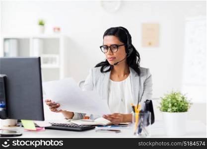 communication, business, people and technology concept - businesswoman or helpline operator with headset, computer and papers at office. businesswoman with headset and computer at office