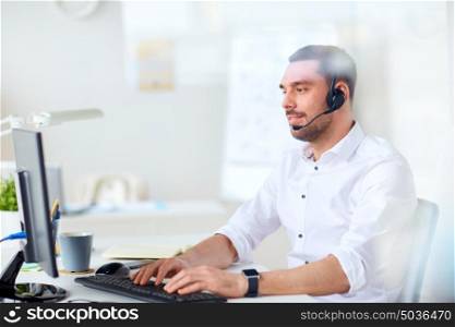 communication, business, people and technology concept - smiling businessman or helpline operator with headset and computer typing at office. businessman with headset and computer at office
