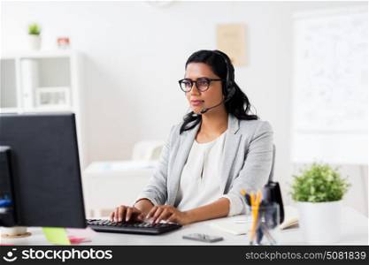 communication, business, people and technology concept - smiling businesswoman or helpline operator with headset and computer typing at office. businesswoman with headset and computer at office