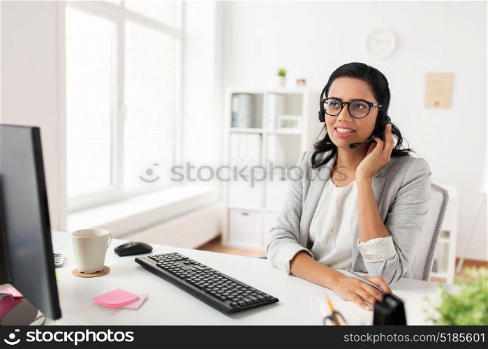 communication, business, people and technology concept - smiling businesswoman or helpline operator with headset and computer talking and typing at office. businesswoman with headset and computer at office
