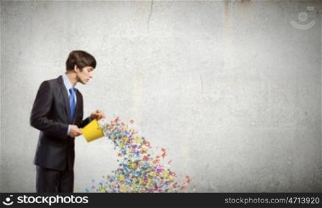 Communication concept. Young businessman holding yellow bucket with colorful letters