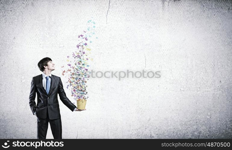 Communication concept. Young businessman holding yellow bucket with colorful letters