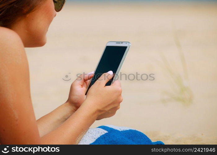 Communication concept. Young woman spending time on summer beach texting messages on smartphone. Girl using mobile phone.. Woman on beach texting on smartphone.